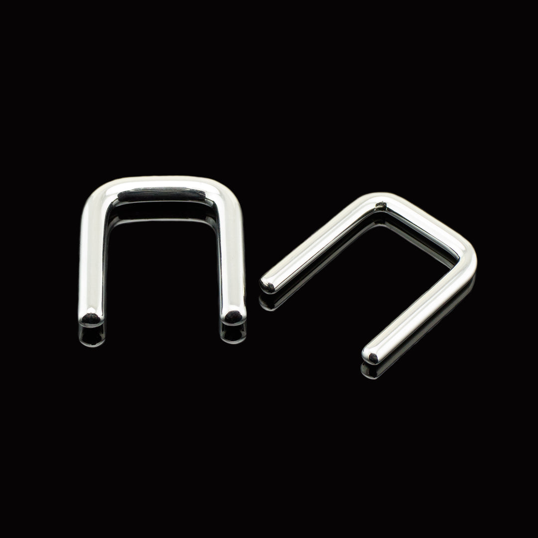 Two titanium staple shaped pieces of body jewelry on a black background.