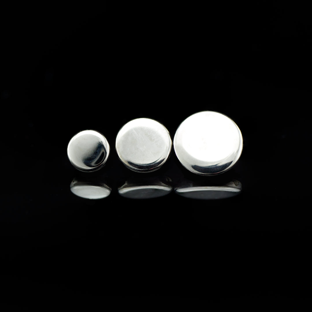 Three round, silver color pieces of body jewelry displayed on a black background.