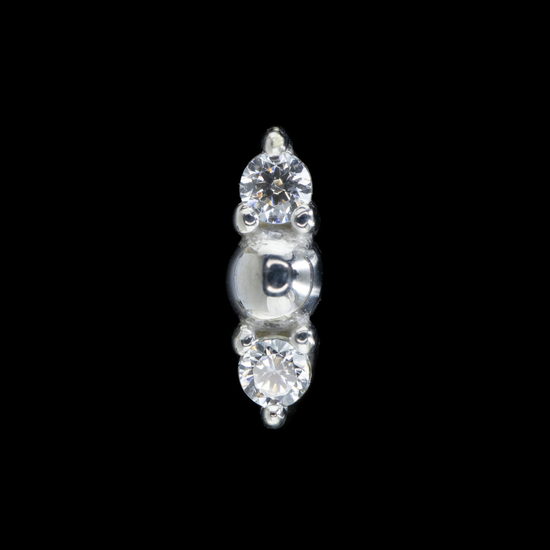 White gold piece of jewelry on a black background. Threadless style with a white gold bead center and 2 clear CZ accents set in prongs.