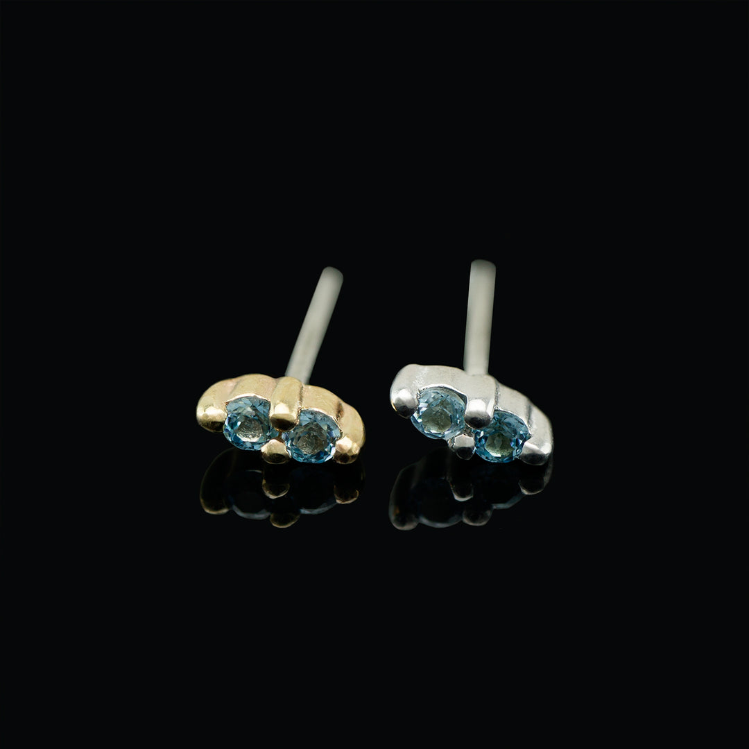 A pair of gold and silver jewelry pieces with two light blue topaz stones set in each.