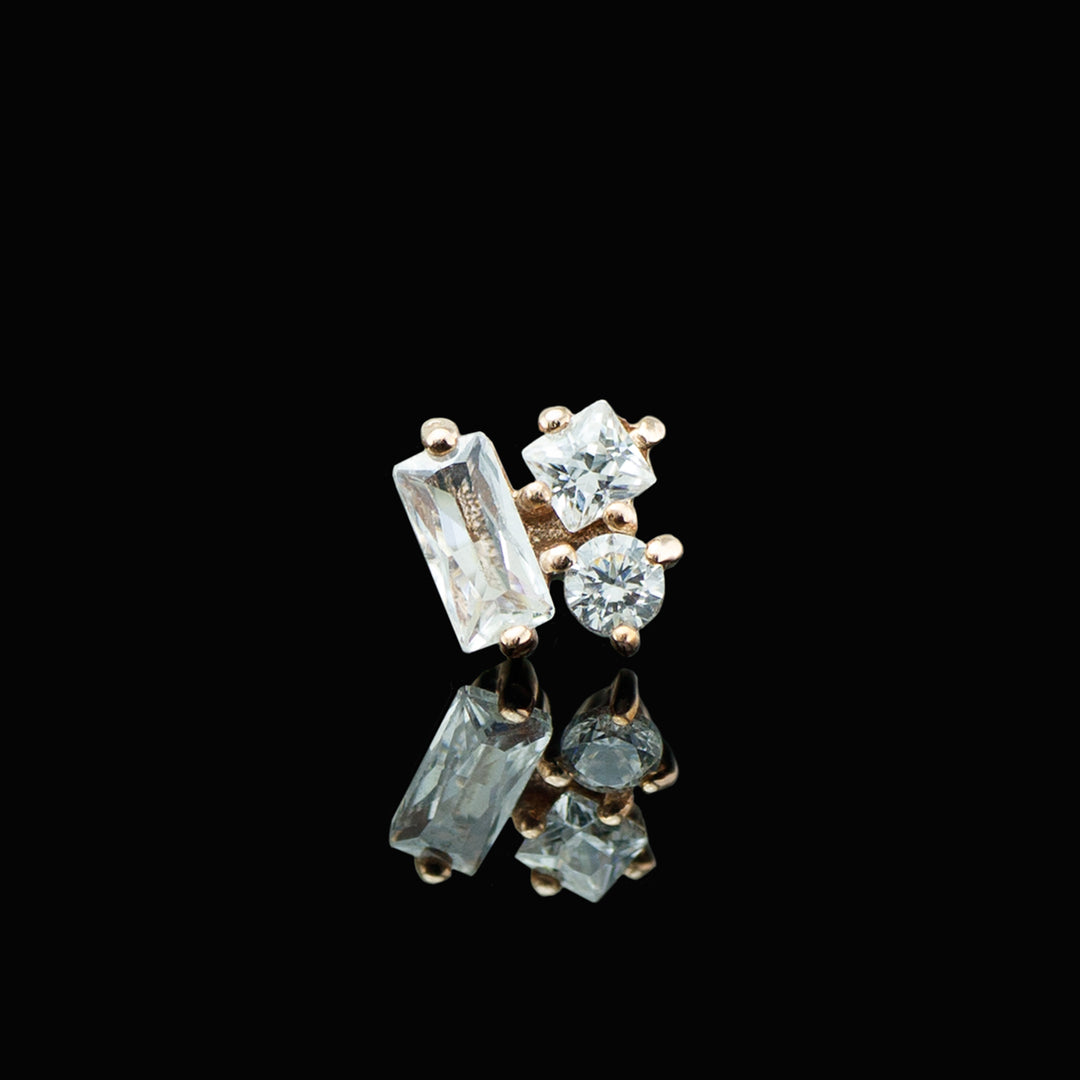 Rose gold piece of body jewelry with a baguette cut, square cut, and round cut white cz set in prong next to echother. Shown on a black background.