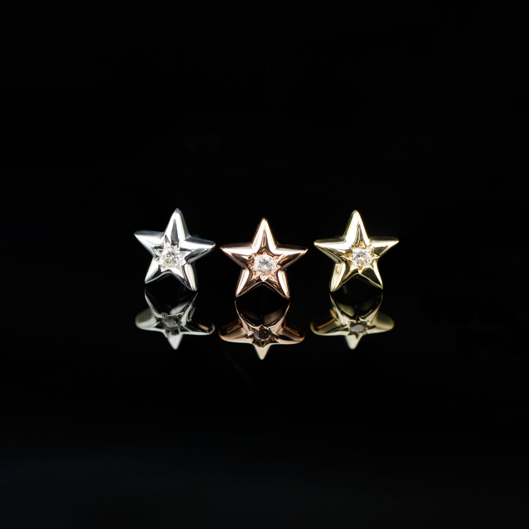 Three five pointed star body jewelry pieces on a black background. These pieces have a small white cz set in the center. Pieces displayed on a black background.