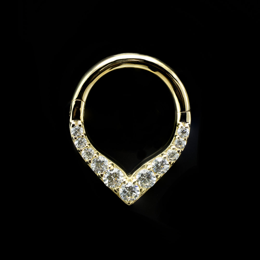 A yellow gold piece of body jewelry on a black background. This is a hinge style ring. The design consists of a solid gold ring, rounded at the top and coming to a point at the bottom, creating a V shape. There are eleven white Swarovski Cubic Zirconia set in prongs along the V shape with the largest stone at the center of the point and descending sizes going up the ring.