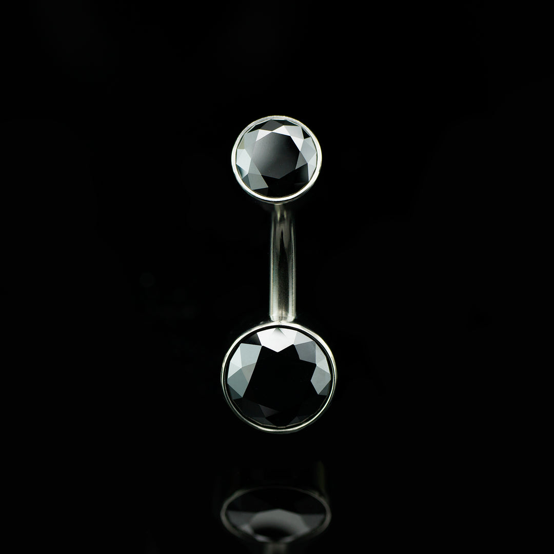 Belly button ring with black gemstones on a black background
