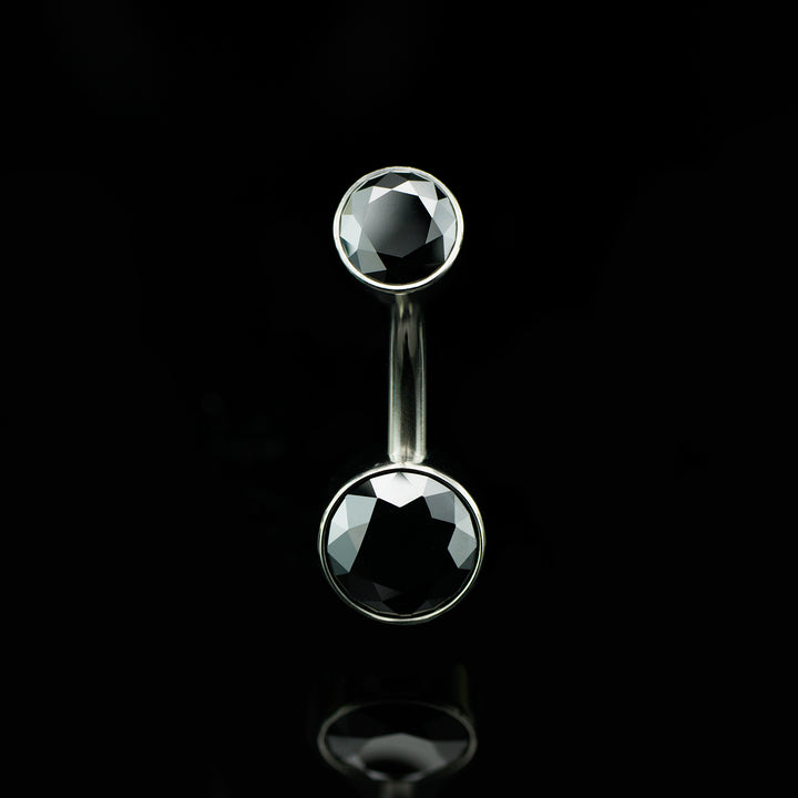 Belly button ring with black gemstones on a black background