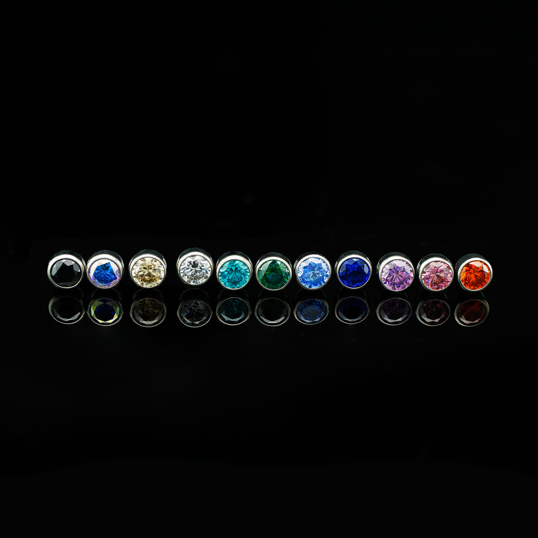 Row of bezel set cubic zirconia in various colors on a black background.