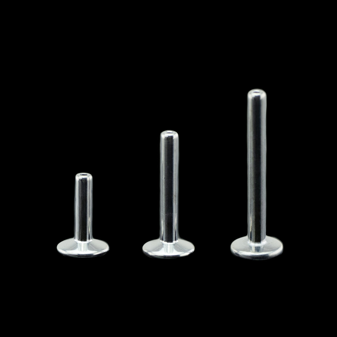 Three flat back push pin style posts on a black background. pictured from left to right in ascending lengths to show the range of sizes. These posts have a larger disk back making them great for piercings that need a little more stability such as cartilage piercings or piercings with larger threadless ends. 
These post are high polished to a mirror finish.
