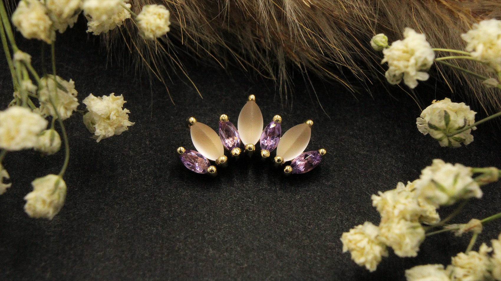 Gold piece of jewelry from BVLA on a black background with flower props. 