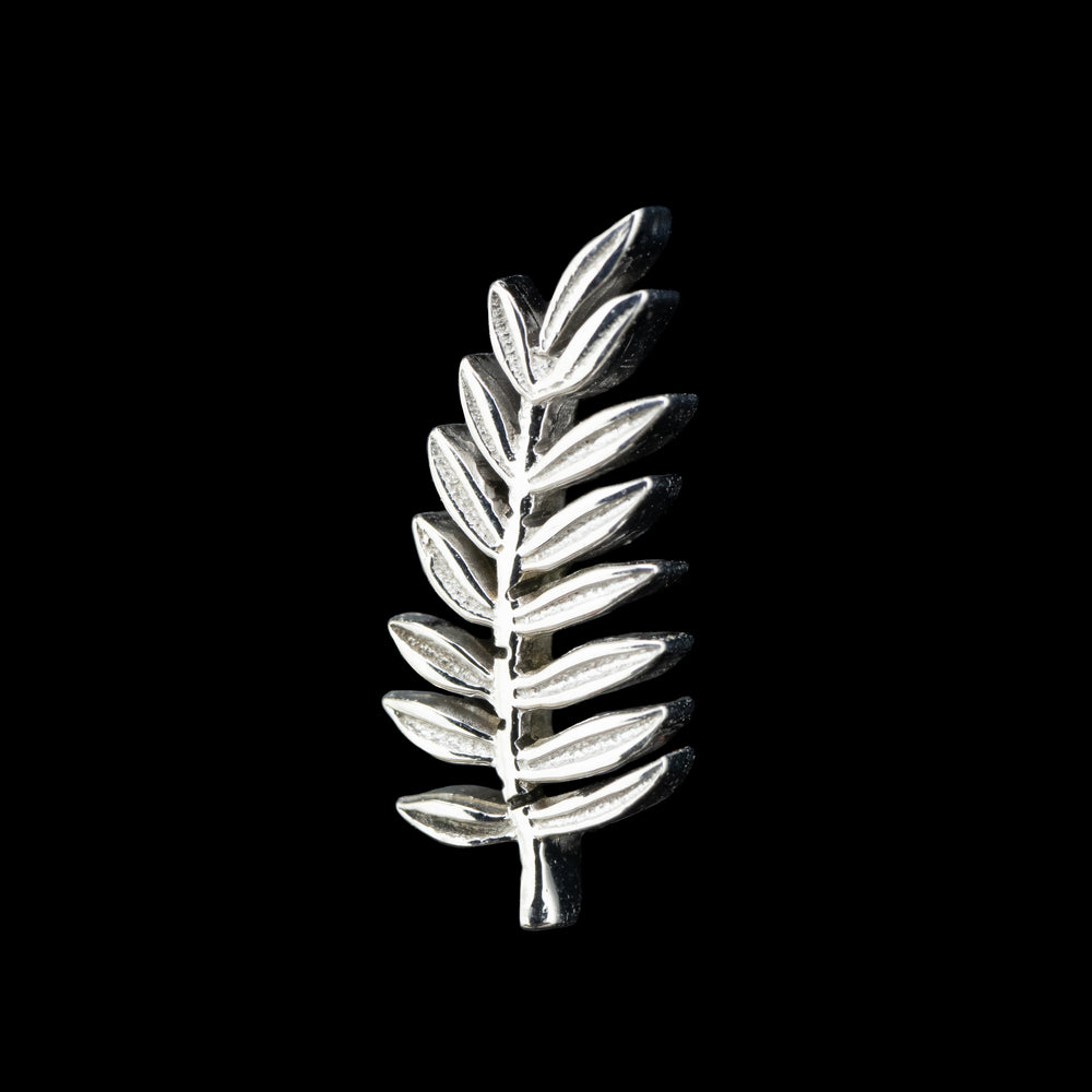  A white gold piece of fine body jewelry on a black background. This is a larger piece of jewelry designed after a branch of a fern. Consists of a stem and 7 thin leaves on either side with a leaf at the top of the piece.  