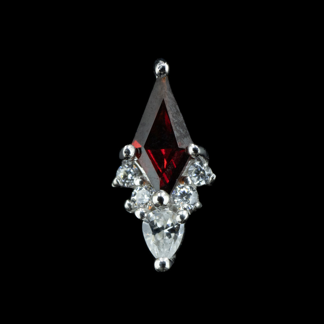 A piece of body jewelry that is a cluster of six gems set in white gold prongs. At the center is a large kite cut garnet with 5 cubic zirconia lining the bottom two sides of the cut kite garnet. the center and lowest cz is a smaller pear cut white cz facing downwards. there are two smaller round cut white czs on either side of the pear cut cz. 