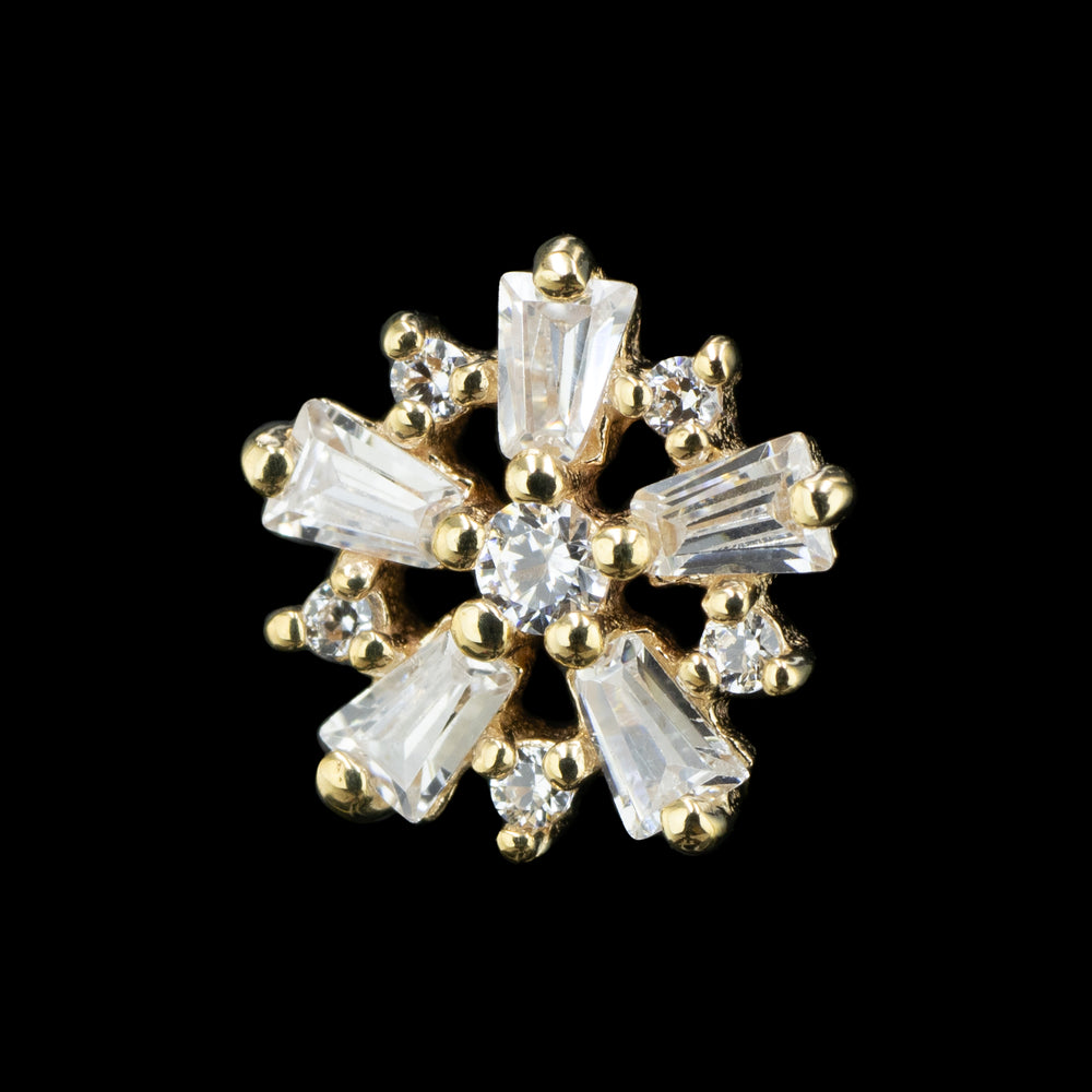 A yellow gold flower shaped piece of body jewelry, Made up of tapered baguette cut and round cut Swarovski Cubic Zirconia on a black background