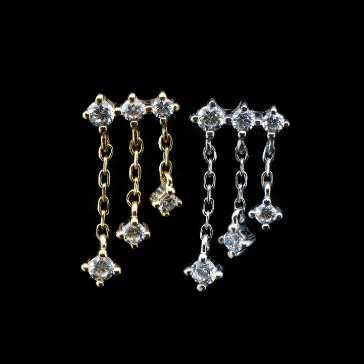 Two Cascade ends on a black background , one in yellow gold and one in white gold. This design consists of three small gems in a row with a length of chain and gem at the end hanging from each.