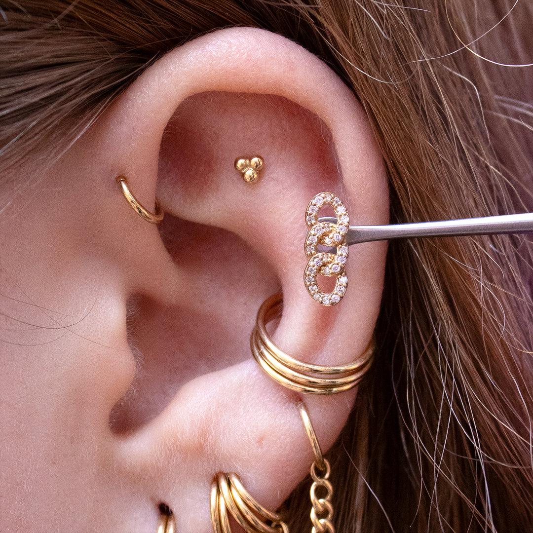 Close-up of an ear with multiple gold earrings including the chainlink end shown in a helix piercing.
