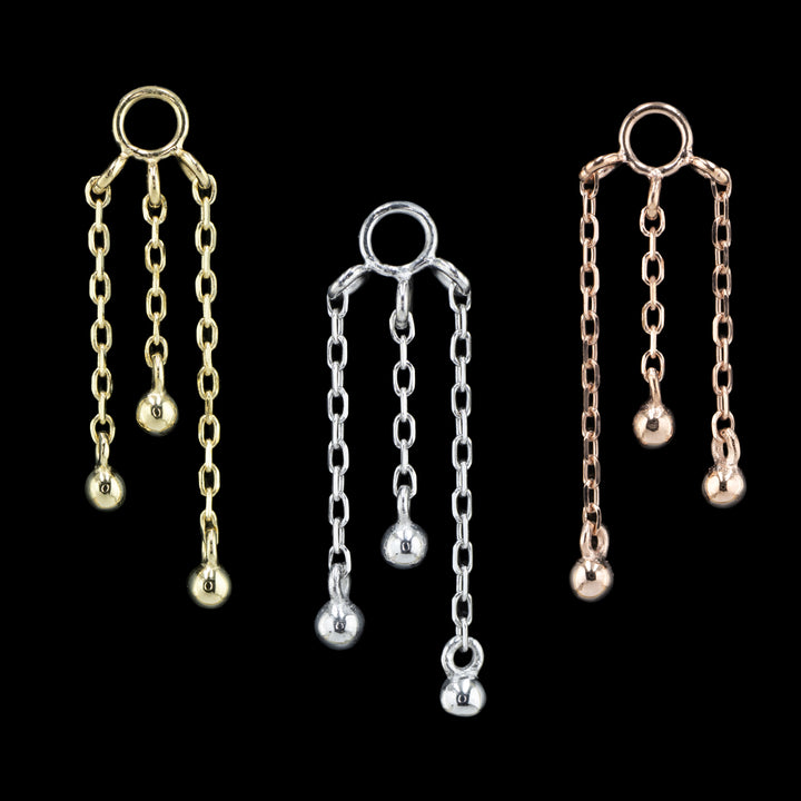 3 body jewelry charms on a black background. The one on the left is yellow gold, the center is rose gold, and the right is white gold. This piece features three varying lengths of cable chain with a small gold bead attached to bottom of each chain.  