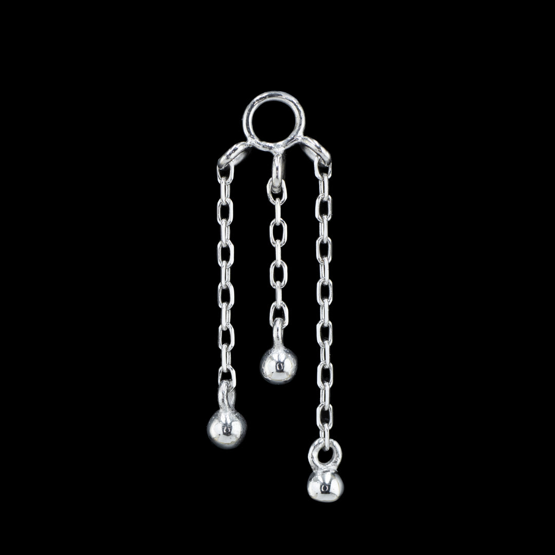 a white gold piece of body jewelry on a black background. This piece features three varying lengths of cable chain with a small gold bead attached to bottom of each chain.  