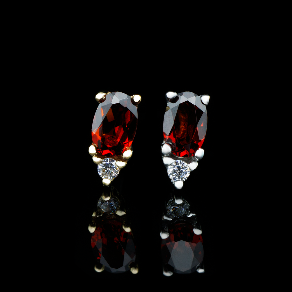Two Desden ends with garnet on a black background. The Desden end is comprised of a larger oval cut garnet with a small round cut Swarovski crystal set below it, all set in solid gold prongs. 
