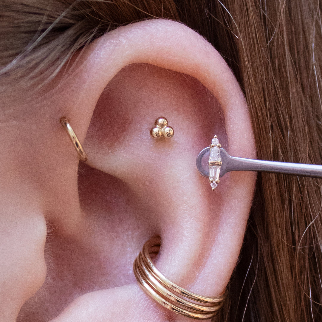 Close up of the upper half of an ear with multiple piercings wearing gold jewelry. Including the Essential, 3 bead cluster, and 18 gauge seam rings.