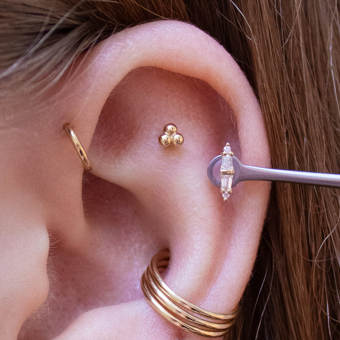 Close up of the upper half of an ear with multiple piercings wearing gold jewelry. Including the Essential, 3 bead cluster, and 18 gauge seam rings.