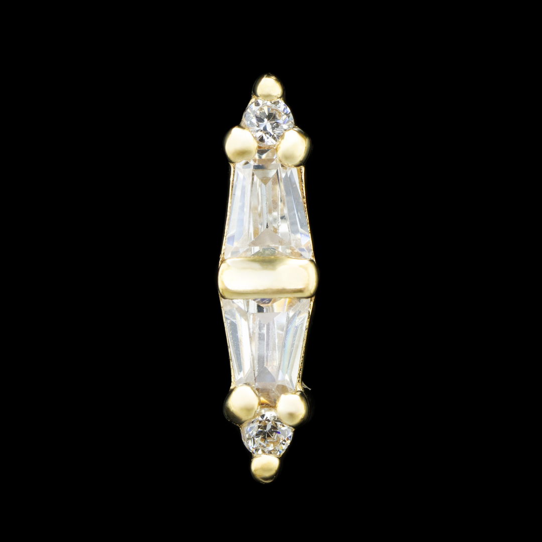 A yellow gold threadless piece of body jewelry on a black background. There are four cubic zirconia set in prongs with a center channel in a column. At the top there is a small round cut CZ with two tapered baguettes at the center with the wider sides of the taper facing each other, and a small CZ at the bottom. 
