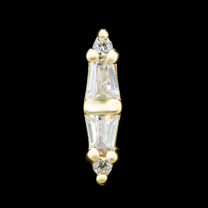 A yellow gold threadless piece of body jewelry on a black background. There are four cubic zirconia set in prongs with a center channel in a column. At the top there is a small round cut CZ with two tapered baguettes at the center with the wider sides of the taper facing each other, and a small CZ at the bottom. 