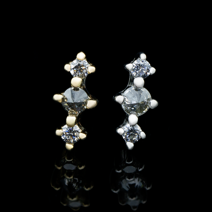 Two ghost flower ends on a black background, one in yellow gold and one in white gold. This design consists of a reverse set grey diamond with two cubic zirconia on either side of it, creating a row of three gems.