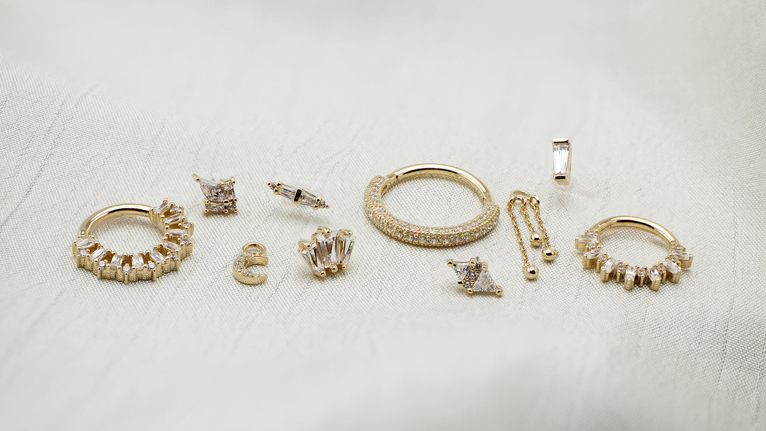 An assortment of yellow gold jewelry from Buddha Jewelry on a white fabric background.