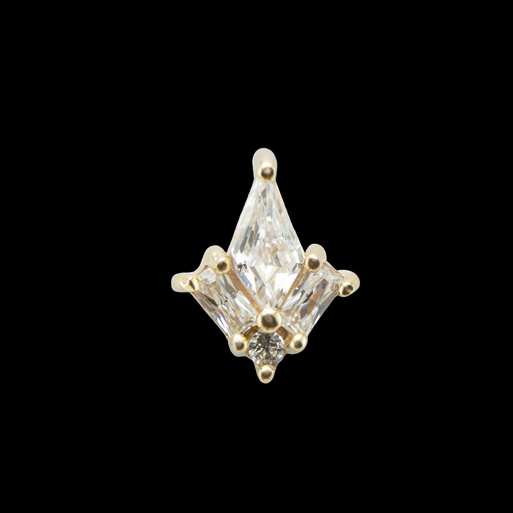 A yellow gold piece of body jewelry on a black background. This piece consists of a kite cut cz at the center with two baguette cut cubic zirconia with the elongated sides flanking the bottom sides of the kite cut cz. A small round cut cz is nestled at the bottom of the piece in the space created by the baguette cut stones. 