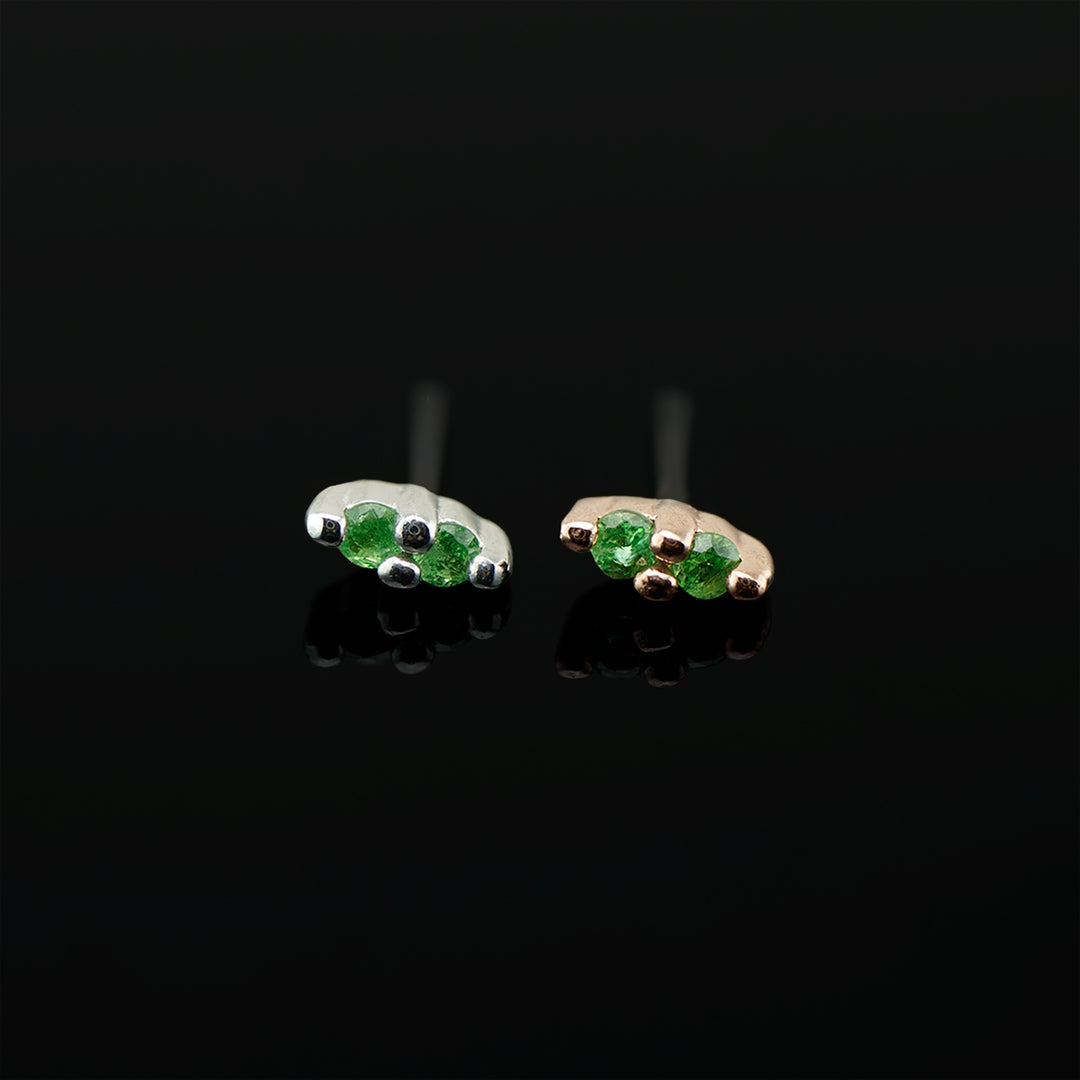 Pair of white gold and rose gold pieces of jewery with two green stones in each. Set on a black background.