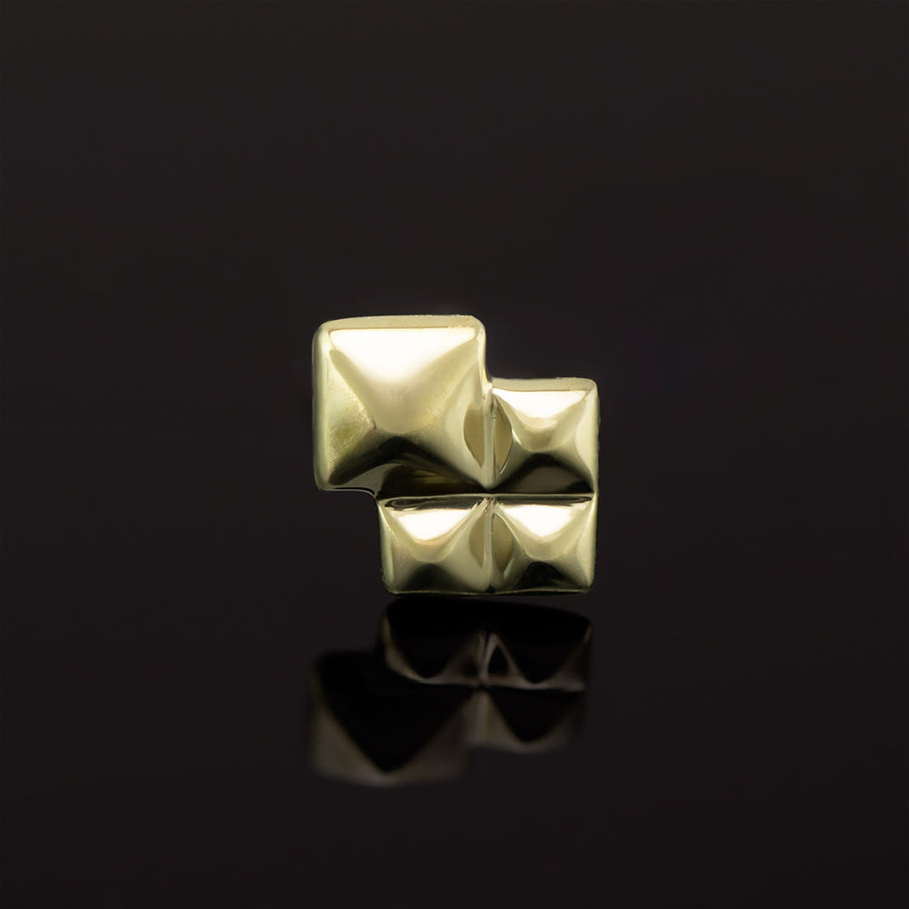 A yellow gold piece of body jewelry on a black background. The design is a larger pyramid shape with three smaller pyramid shapes clustered around two sides. 