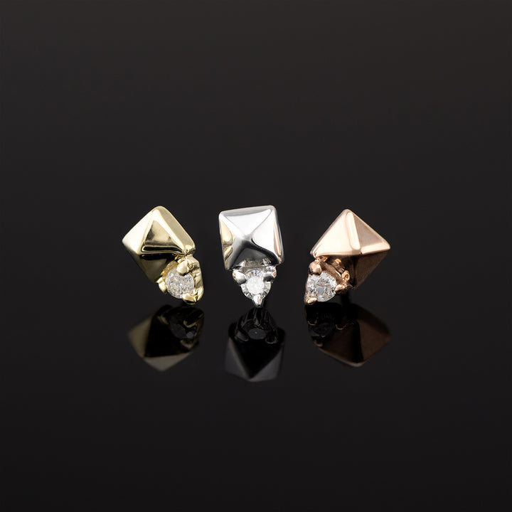 Three pieces of push pin body jewelry made of solid gold. From left to right we see a piece in yellow gold, rose gold, and white gold. All are 14k gold. The design is a pyramid shape made of gold with a genuine diamond set in three prongs on one side.