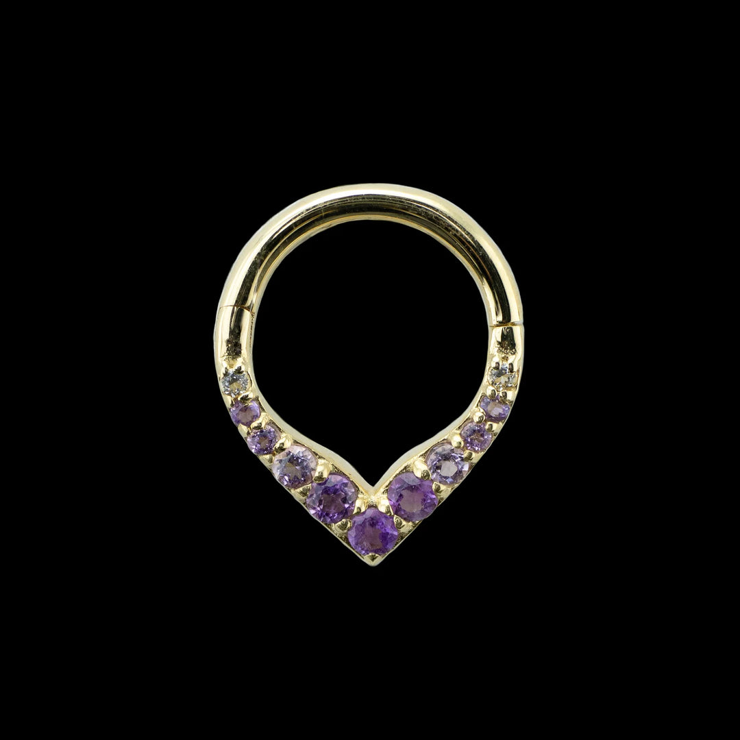 A yellow gold piece of body jewelry on a black background. This image shows a front view of this design. It is a V shaped hinge body ring with 11 round cut amethyst set into the v. At the bottom point is a larger sized amethyst with smaller descending sizes going up the hoop. The center largest 3 gems are the deepest in color and they fade to a lighter purple as they go up the ring.  