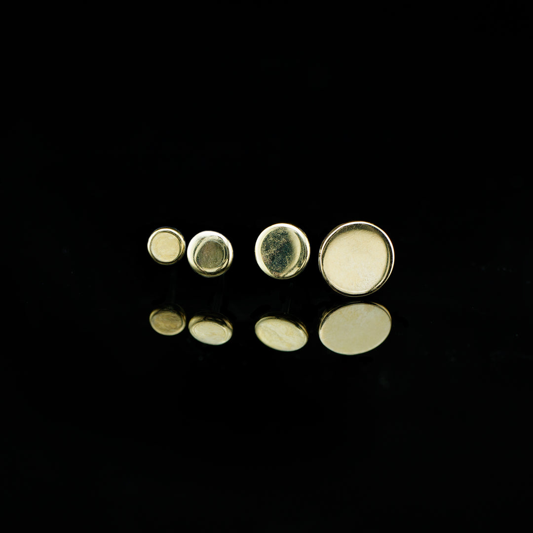 A row of yellow gold round disk ends in ascending sizes on a lack background.