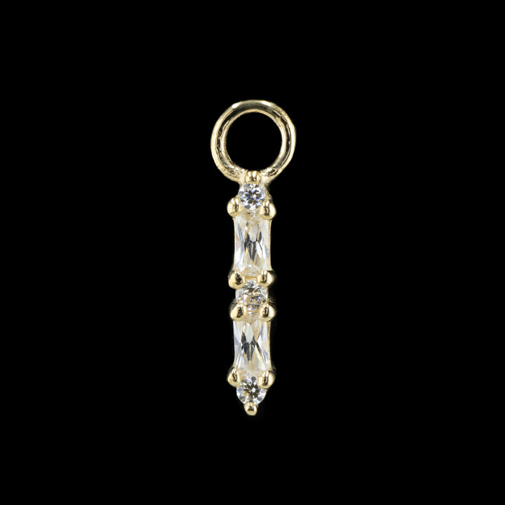 yellow gold charm on a black background. The piece features 5 swarovski cubic zirconia in a row. There are three round cut white CZs and 2 baguette cut white CZs in an alternating column starting with the round cut cubic zirconia. 