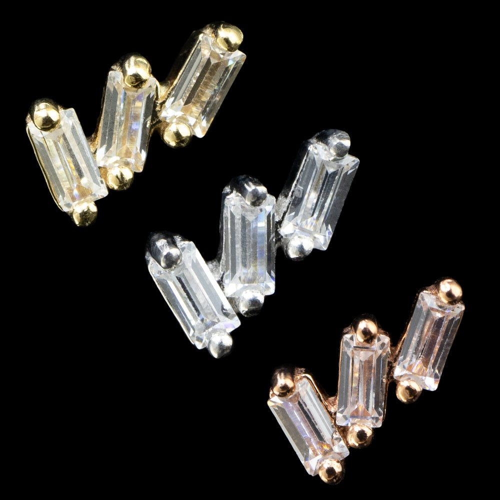 3 pieces of gold body jewelry on a black background. Each piece is made up of 3 baguette cut clear stones offset next to each other and each one leaning more to the right.