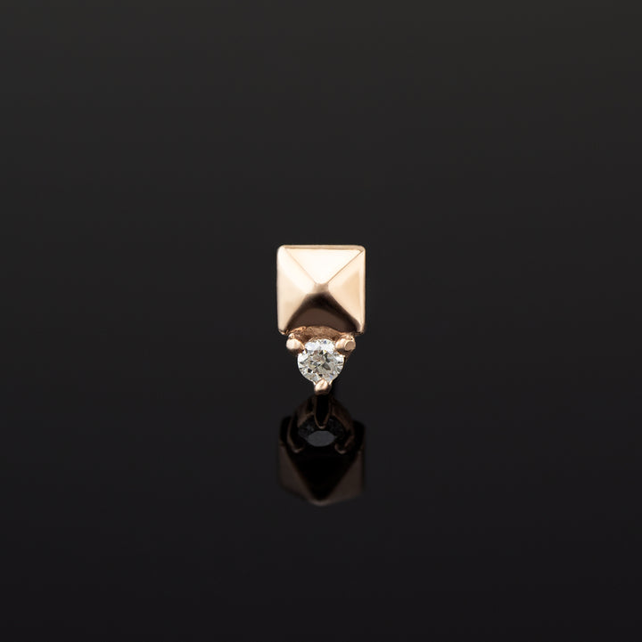 A push pin piece of rose gold body jewelry made of solid 14 karat gold. The design is a pyramid shape made of gold with a genuine diamond set in three prongs on one side.