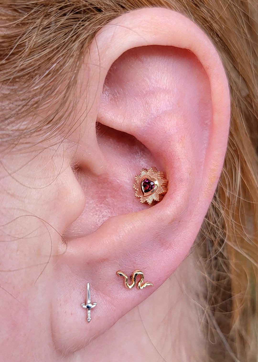 Close up of an ear with 2 earlobe piercings wearing Blade and Serpent ends from Buddha jewelry along with a Milagro end with Rhodolite garnet in yellow gold. 