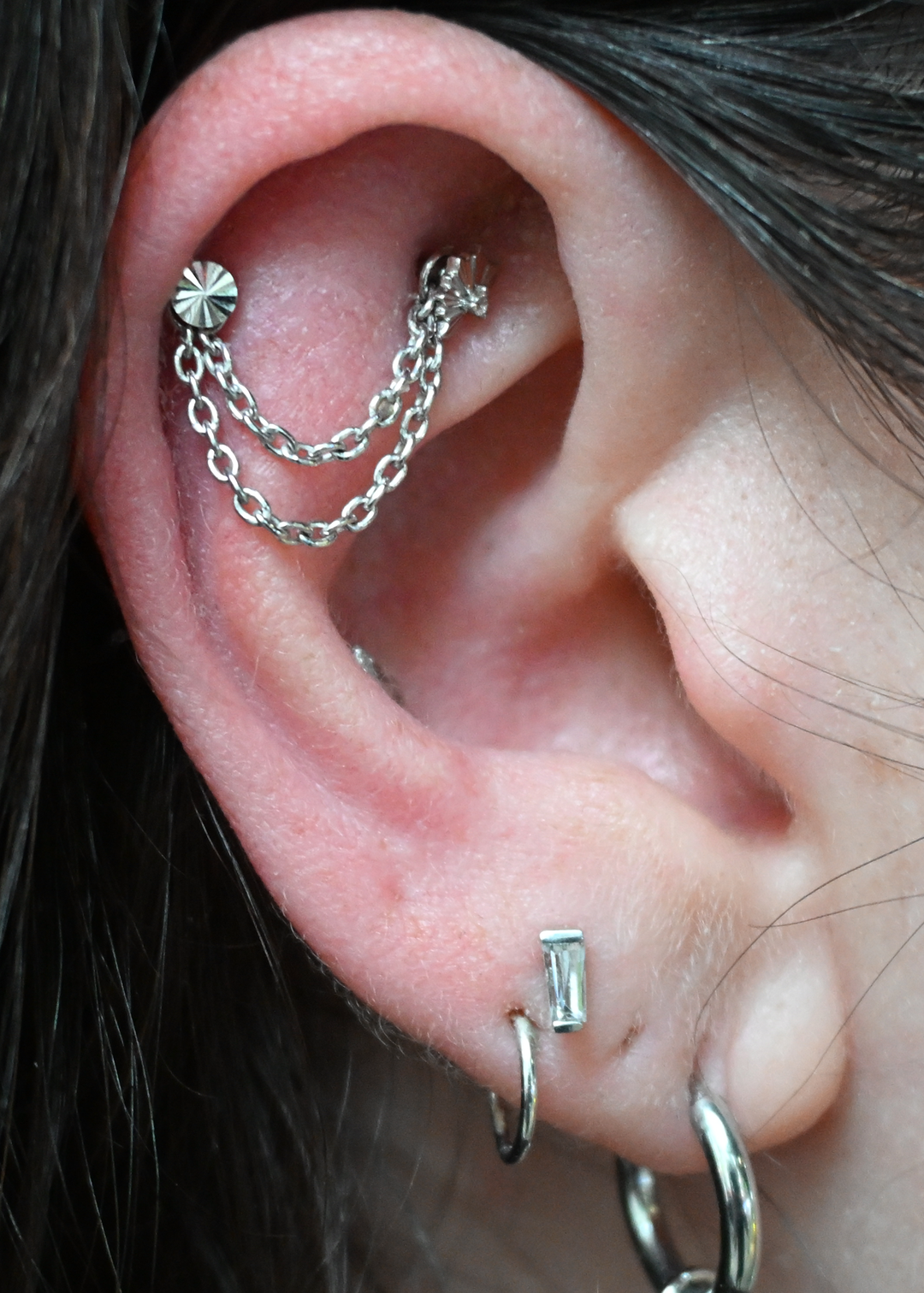 Close up of an ear with helix, flat, and earlobe piercings. Wearing a Lazer Disk end and a Tapered Baguette end from Buddha Jewelry in white gold. 