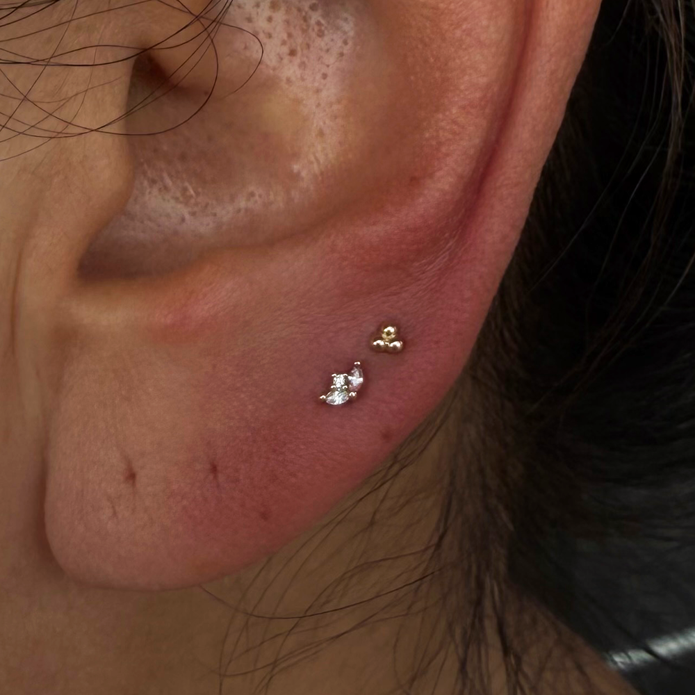 Close up of an ear with two earlobe piercings. One with a yellow gold Pur threadless end and the other wearing a standard 3 Bead Threadless End from Buddha Jewelry.