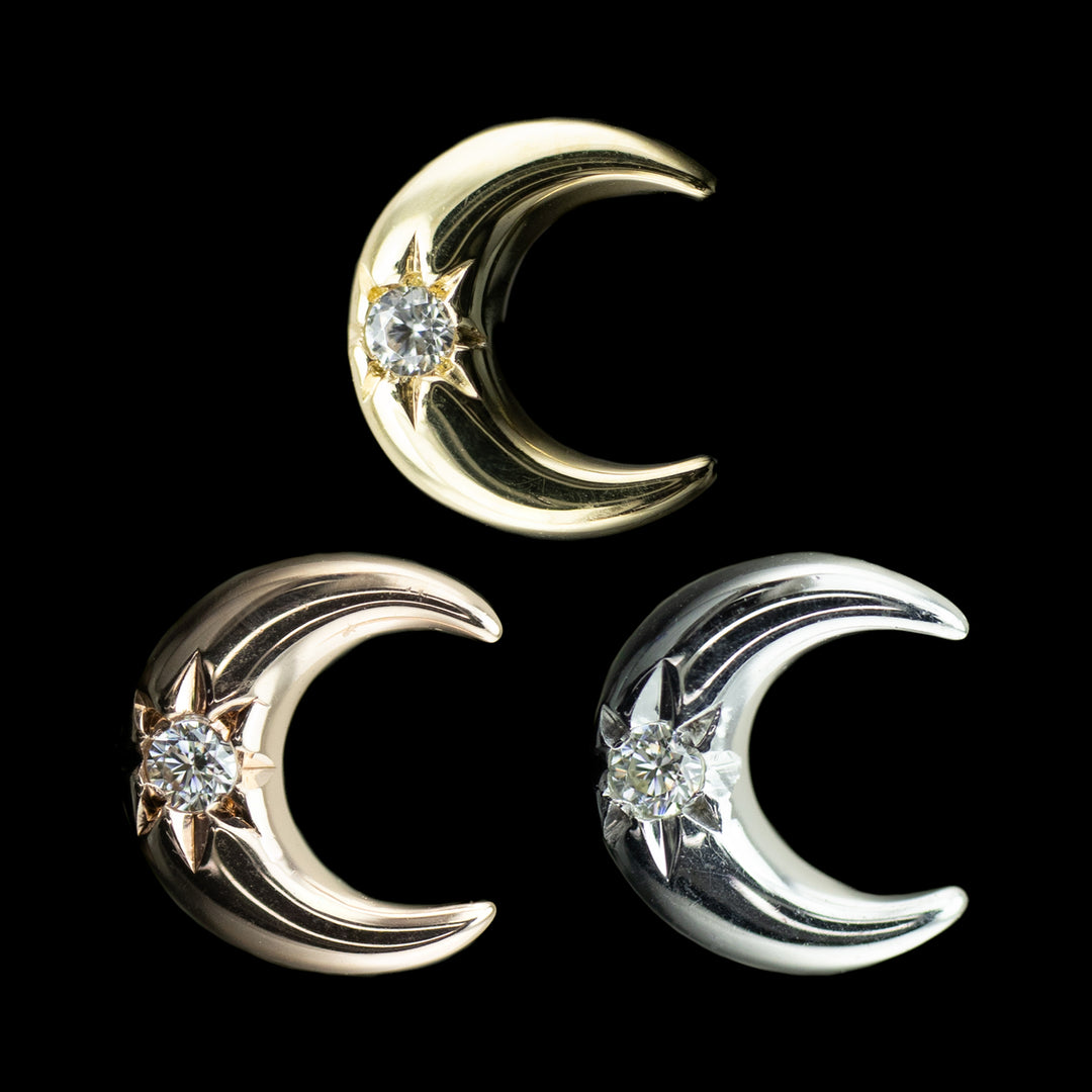 3 Gold jewelry pieces shaped like moons with a white cubic zirconia center on a black background. one moon is yellow gold, one is rose gold, and one is white gold. 