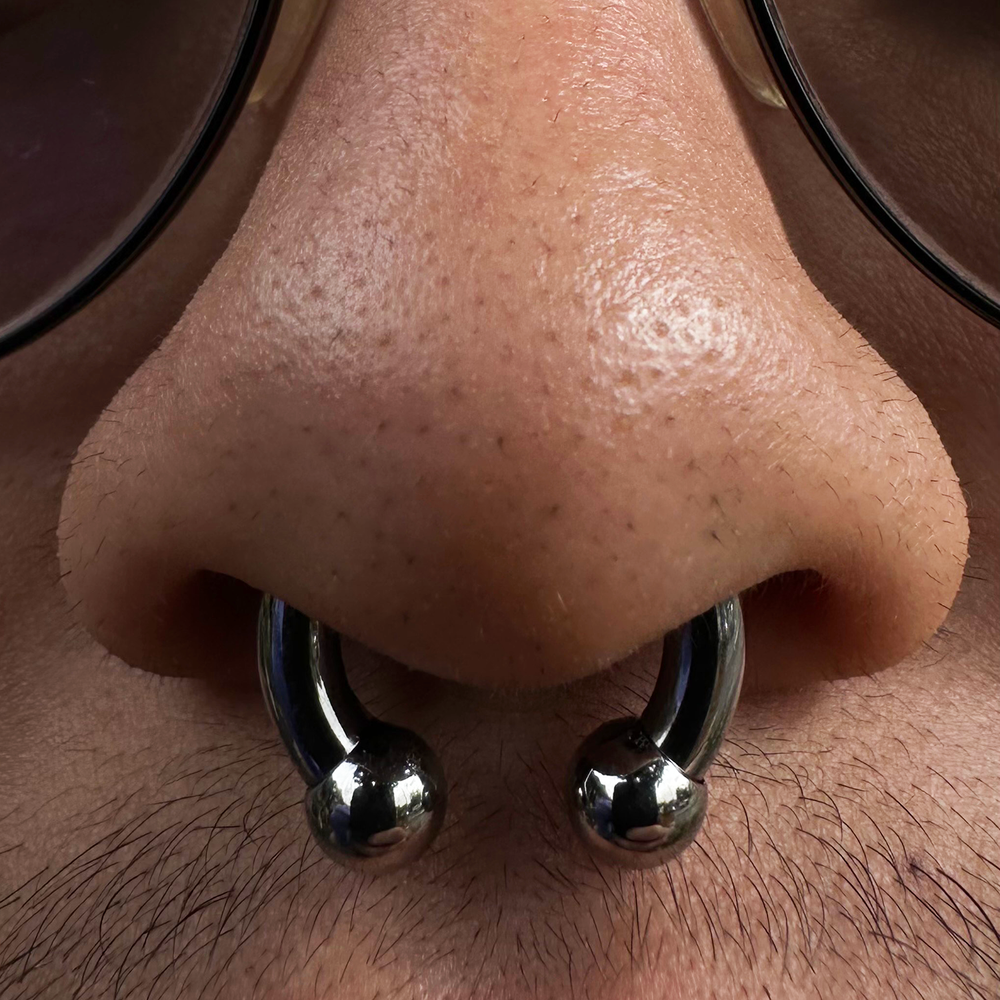 A close up of a septum piercing wearing a larger gauge circular barbell in implant grade titanium. 
Horseshoe septum piercing.
