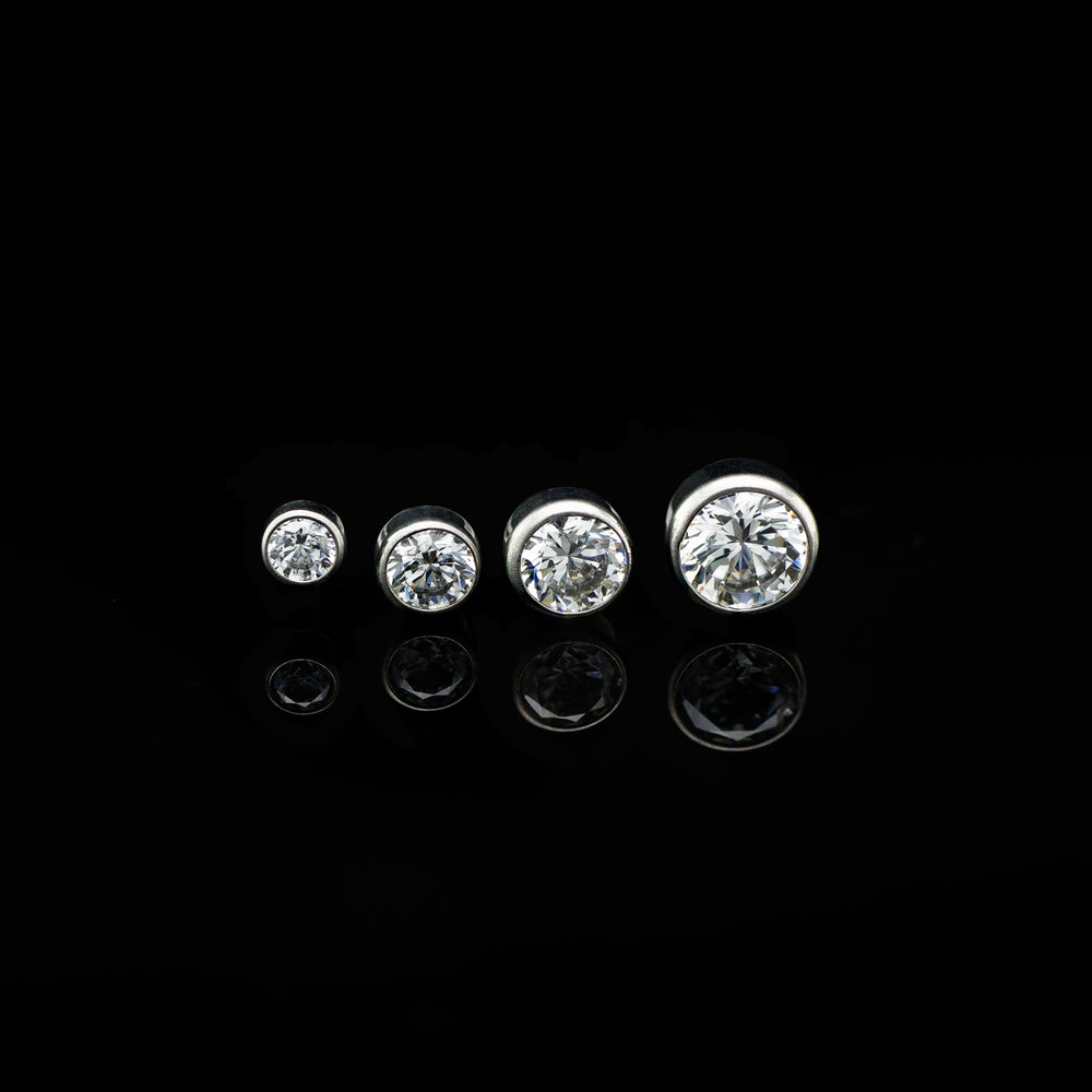 Row of four bezel set white cubic zirconia in varying sizes on a black background.