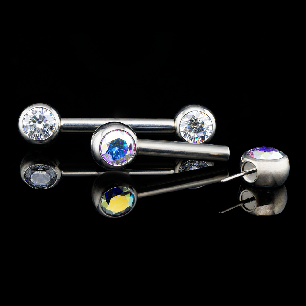 Two sets of nipple jewelry consisted of the side set gems and a push pin nipple barbell on a black background. 

