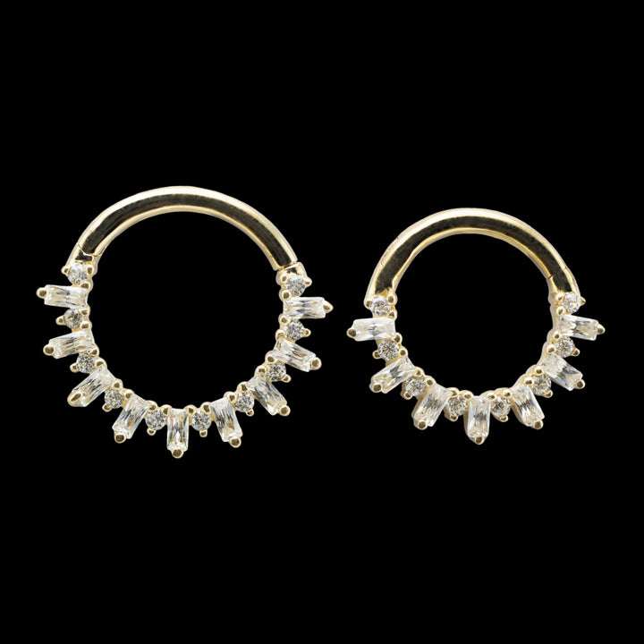 Two yellow gold pieces of body jewelry on a solid black background. The piece is a clicker hinge style ring with a high polish yellow gold wearing surface. The design of the ring consists of alternating round cut and baguette cut swarovski cubic zirconia. 