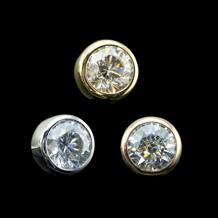 3 bezel set cubic zirconia in varying gold tones on a black background. one piece is yellow gold, one is rose gold, one is white gold. earrings for cartilage piercings, nostril piercings, and conch piercings.