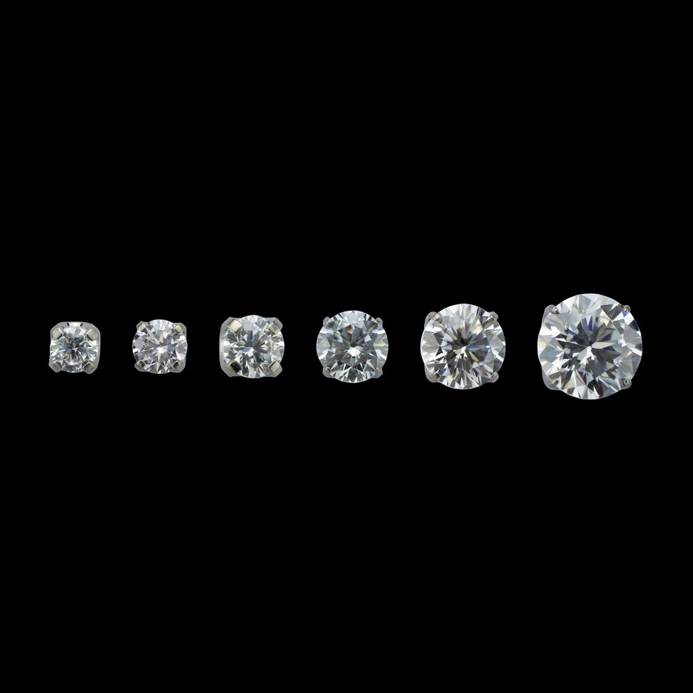 6 pieces of implant grade titanium body jewelry. Shown from left to right in ascending sizes. Each piece is a solitaire white cubic zirconia set in four prongs.  