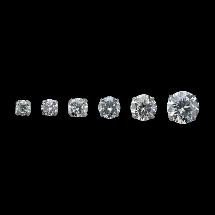 6 pieces of implant grade titanium body jewelry. Shown from left to right in ascending sizes. Each piece is a solitaire white cubic zirconia set in four prongs.  