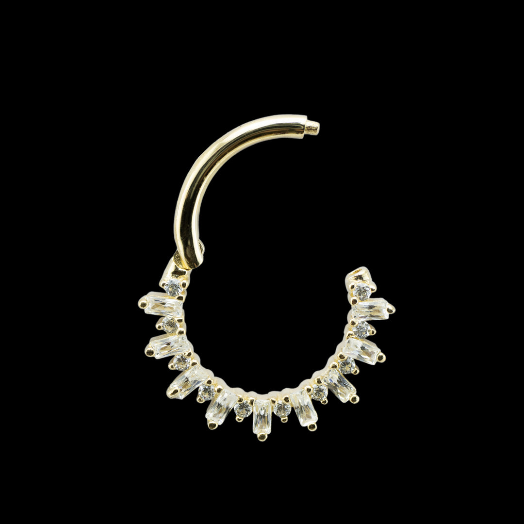 A yellow gold piece of body jewelry on a solid black background. This photo shows the hinge ring open to show off the clicker mechanism. The design is a combination of alternating round cut and  baguette cut swarvski CZs. 