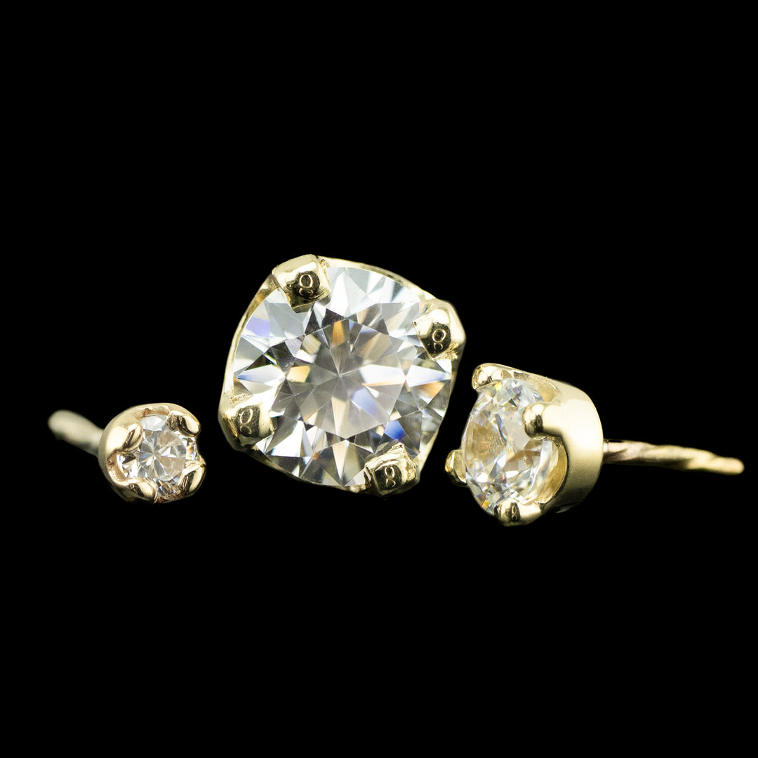 3 varying sizes of white Cubic Zirconia set in a four prong solitaire setting. The pieces pictured are yellow gold on a black background. 