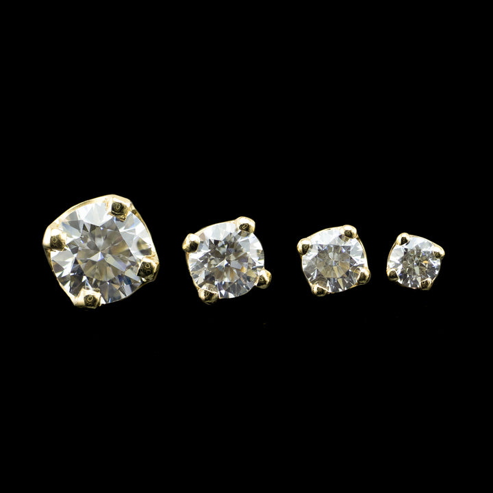 4 varying sizes of white CZ set in a four prong solitaire setting. The pieces pictured are yellow gold on a black background. 